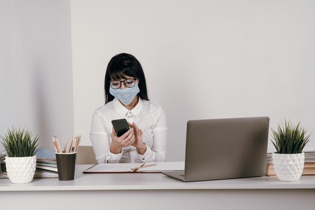 A young woman works remotely in the office with a protective mask during an epidemic