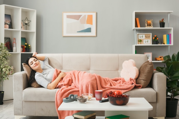 Photo young woman wrapped in plaid lying on sofa behind coffe table in living room