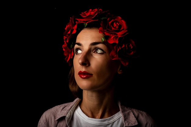 Young woman in a wreath with red flowers looking to the side on a black background.