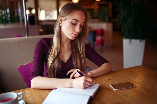 若い女性がカフェで彼女のノートに書く