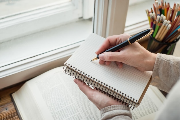 大きな窓の前でメモを書く若い女性