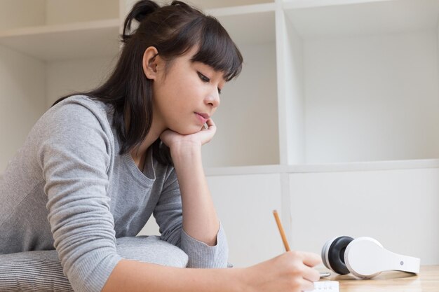 家の床に横たわって書いている若い女性