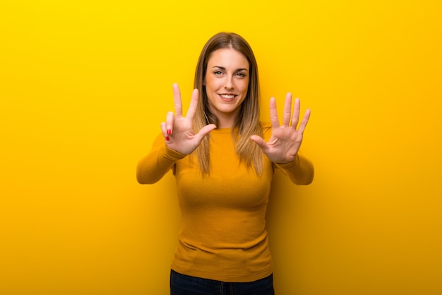 Young woman on yellow background counting eight with fingers