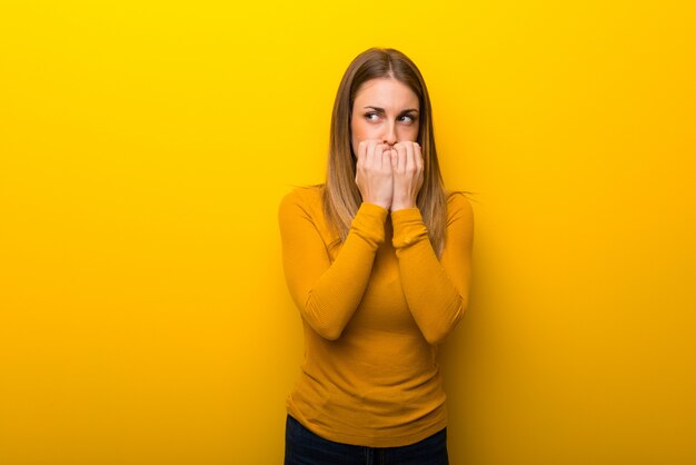 Young woman on yellow background is a little bit nervous and scared putting hands to mouth