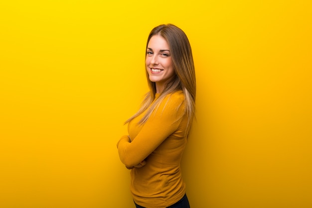 Giovane donna su sfondo giallo mantenendo le braccia incrociate in posizione laterale mentre sorridente