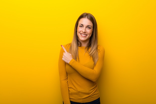 Young woman on yellow background pointing to the side to present a product