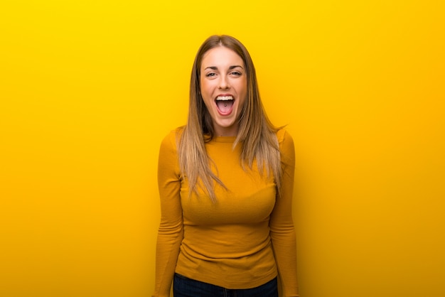 Young woman on yellow background shouting to the front with mouth wide open