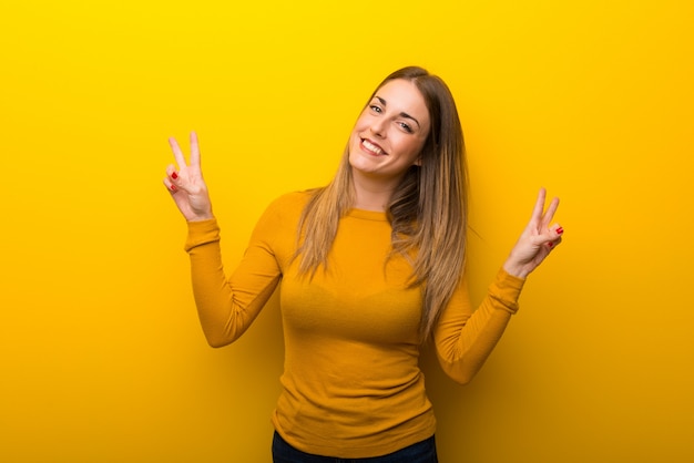 Giovane donna su sfondo giallo, sorridente e mostrando il segno della vittoria con entrambe le mani