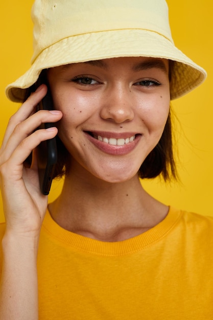 노란색 모자를 쓴 젊은 여성이 캐주얼하게 전화로 격리된 배경에서 이야기하고 있습니다.