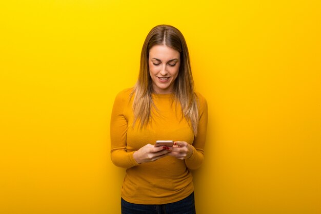 携帯電話でメッセージを送信する黄色の若い女性