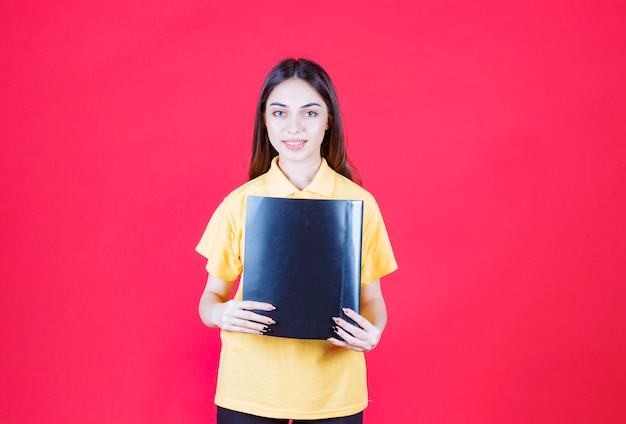 Photo young woman in yellow shirt holding a black folder