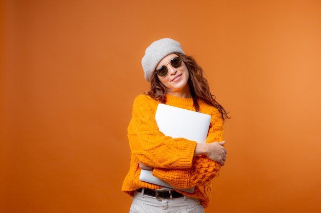 a young woman in a yellow sweater on a yellow background holds a laptop