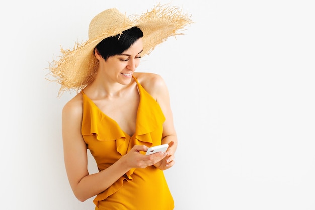 Photo young woman in yellow swimsuit and straw hat using mobile smartphone. summer