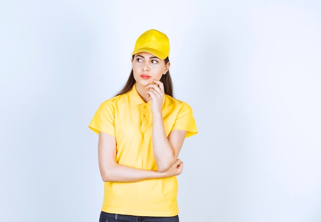 Young woman in yellow t-shirt and cap standing on white background.