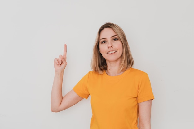 Young woman in yellow t-shirt pointing her finger up. On white background. Hand gestures