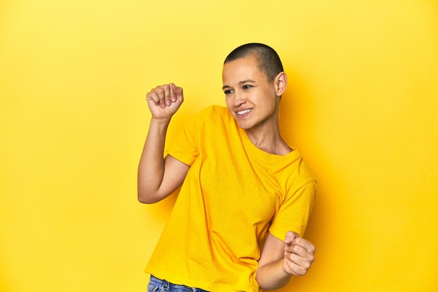 Young woman in yellow tee yellow studio backdrop dancing and having fun