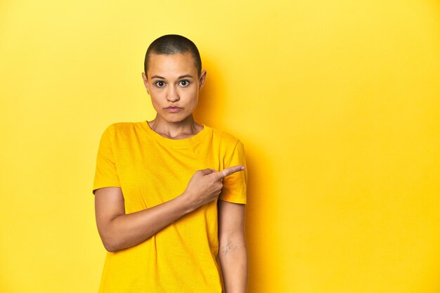 Photo young woman in yellow tee yellow studio backdrop pointing to the side