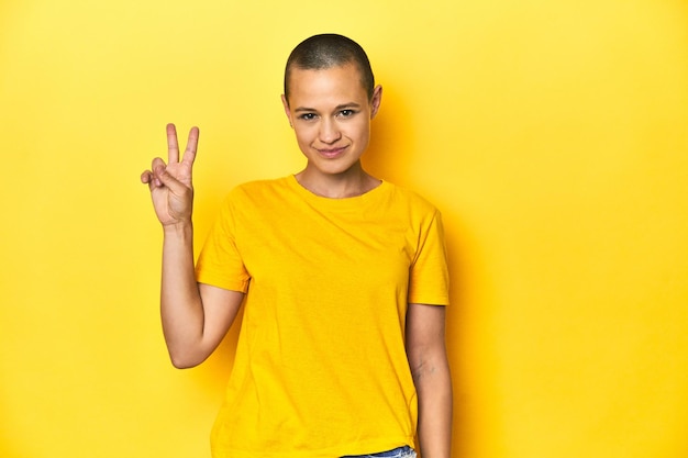 Young woman in yellow tee yellow studio backdrop showing victory sign and smiling broadly