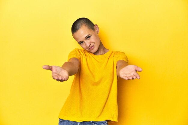 Photo young woman in yellow tee yellow studio backdrop showing a welcome expression