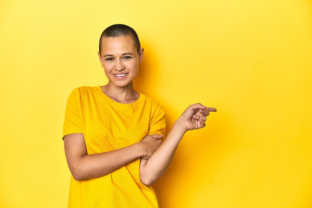 Young woman in yellow tee yellow studio backdrop smiling cheerfully pointing with forefinger away