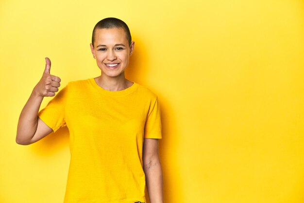Young woman in yellow tee yellow studio backdrop smiling and raising thumb up