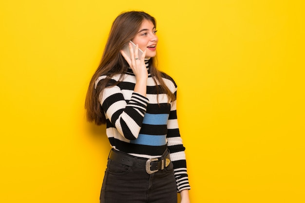 Young woman over yellow wall keeping a conversation with the mobile phone