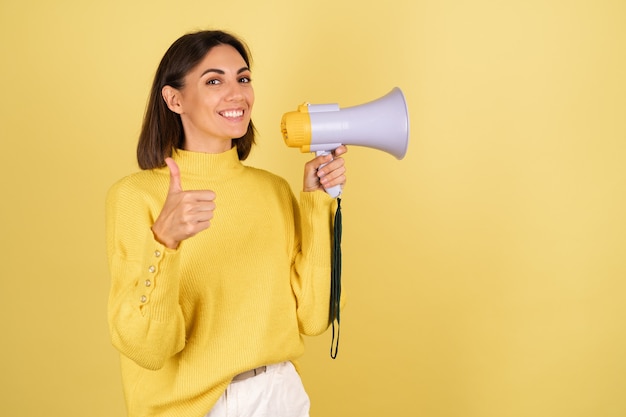 Young woman in yellow warm sweater with megaphone speaker showing thumb up