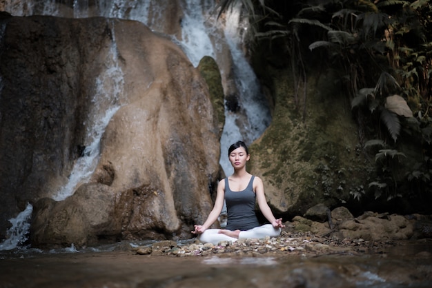 Young woman in yoga pose sitting near waterfall