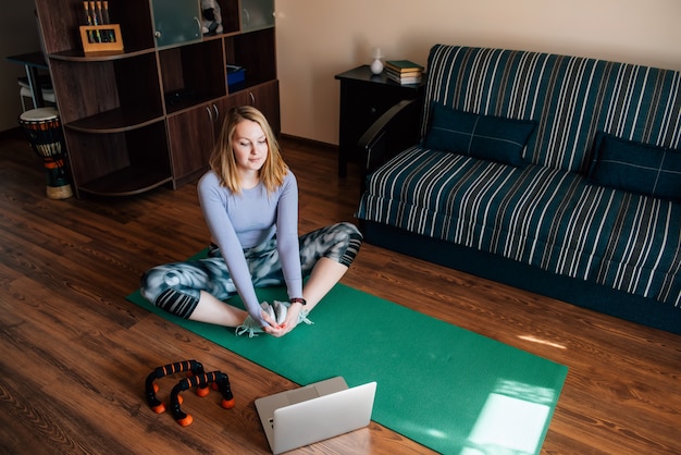 Foto giovane donna nella posa di yoga che guarda classe online nella sala
