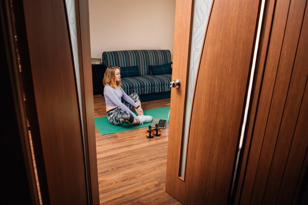 Young woman in yoga pose watching online class in room