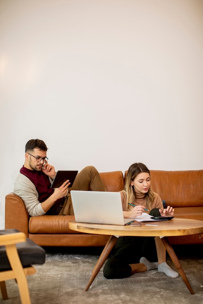 Young woman and young man using laptop while sitting by the sofa at home