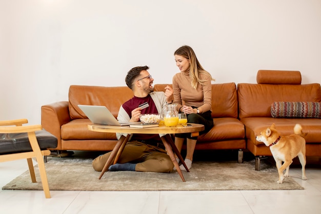 Young woman and young man using laptopfor online payment while sitting by the sofa with their shiba inu dog at home