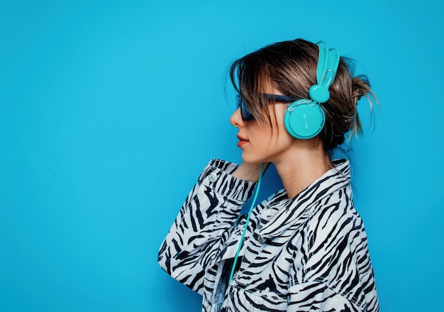 Young woman in zebra clothes and headphones on blue background