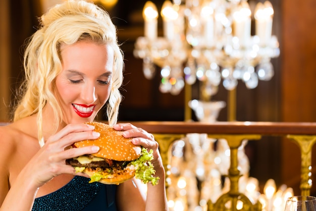 Il giovane ristorante di cucina raffinata mangia un hamburger, si comporta in modo improprio