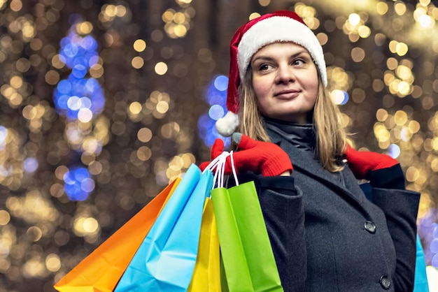 Foto una giovane donna fa shopping a natale con sacchetti di carta colorati e luminosi con regali per festeggiare il nuovo anno