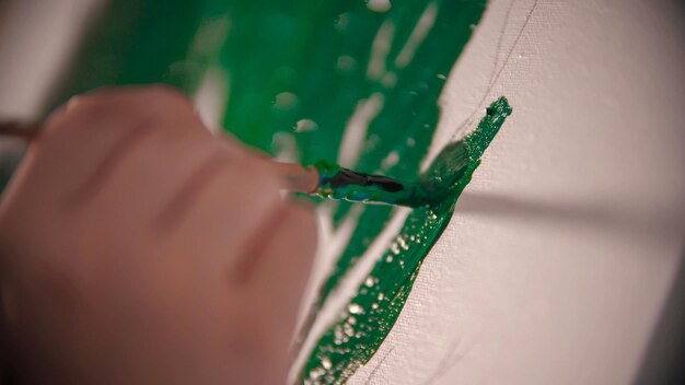 A young womans hand painting a green crown of the tree on the\
canvas