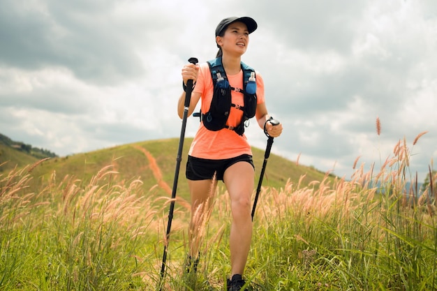 Photo young women active trail running across a meadow on a grassy trail high in the mountains in the afternoon with trekking pole