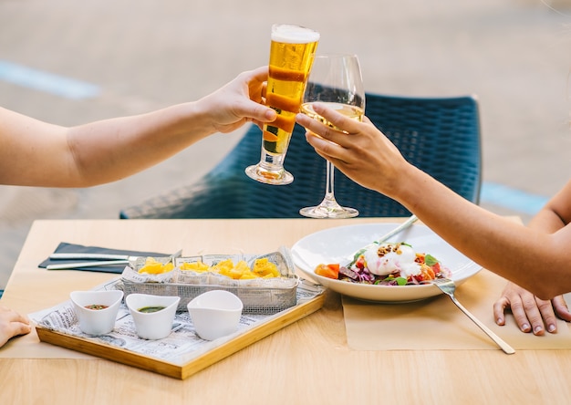 Giovani donne che applaudono birra e mangiano cibo sulla terrazza - due ragazze pranzano insieme in un ristorante