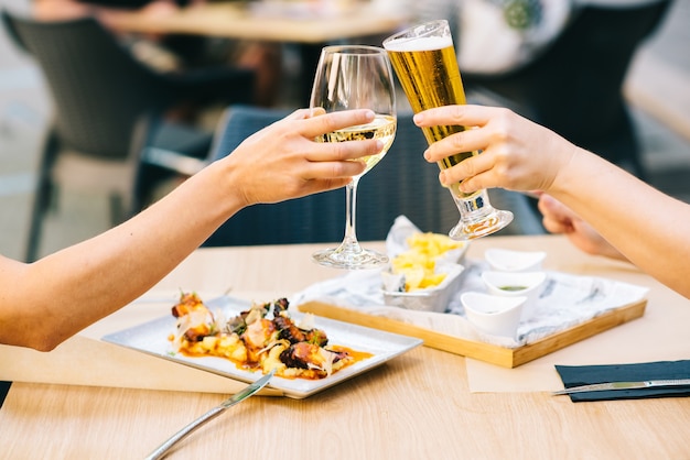 Giovani donne che applaudono birra e mangiano cibo sulla terrazza - due ragazze pranzano insieme in un ristorante