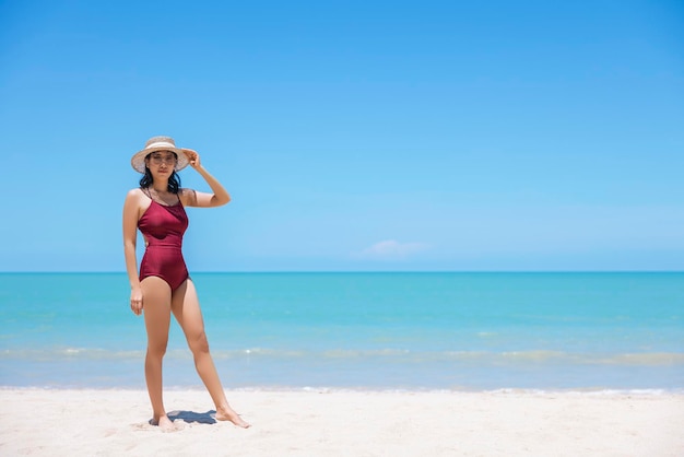 Young women in bikini and straw hat stand on tropical beach enjoying looking view of beach ocean on hot summer day Blue sea in background Khao Lak Phang Nga Thailand Summer vacation concept