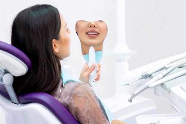 사진 젊은 여성은 거울에서 이빨을 확인합니다. 치과 의사 사무실에서 젊은 여자.