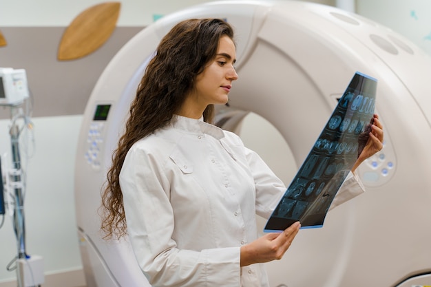 Фото Врач молодой женщины в медицинском халате смотрит на результаты рядом с компьютерным томографом