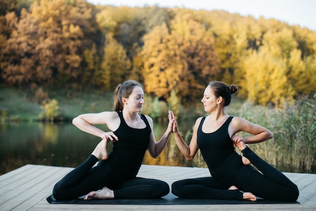 Young women doing yoga asana in nature near the lake