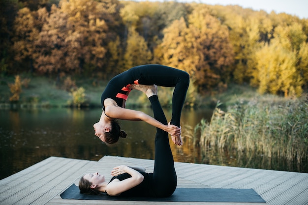 Молодые женщины делают асаны йоги на природе у озера