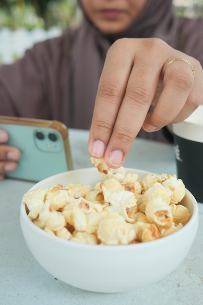 ポップコーンを食べながらスマートフォンを使う若い女性