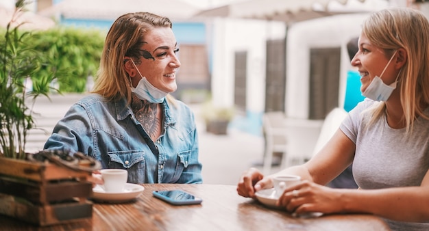 Young women friends drinking coffee at bar during coronavirus pandemic time