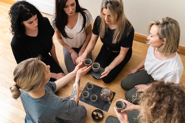 Photo young women friends kneeling around a tray are holding cups of hot tea during a tea ceremony