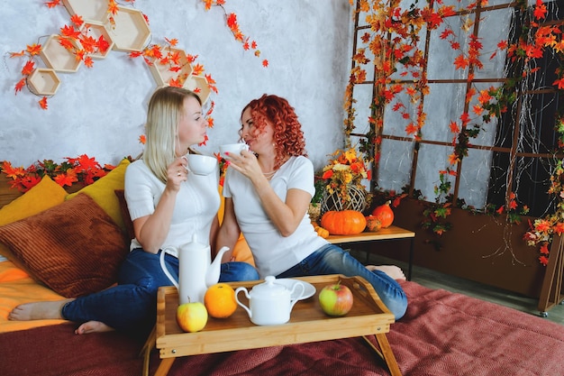 young women, friends, sisters  sitting in cozy bed. tea cups, drinking tea in sweaters. Fall season