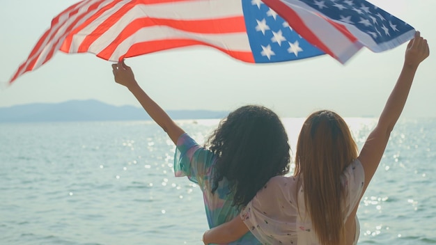 写真 夏休みでビーチや海で アメリカの旗を掲げて 笑顔で休暇を楽しんでいます