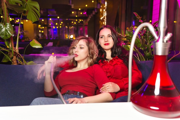 사진 빨간 옷을 입은 젊은 여성들은 물담배 바나 나이트클럽에서 물담배를 피웁니다.